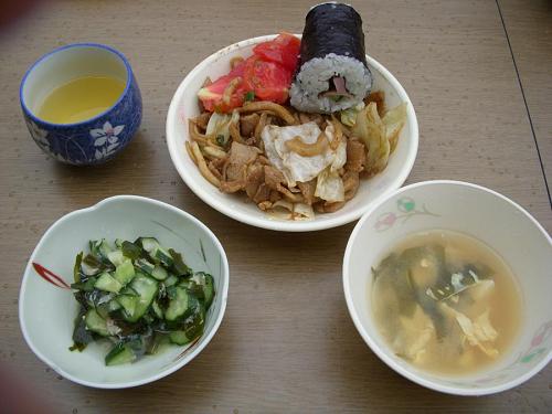 本日のメニューは、チームくんちゃんの焼きそば定食　　具だくさんの焼きそばをメインに、ハム巻き寿司、キュウリとカニ酢のもの、味噌汁、おにぎり、といつもながら彩り豊富です。